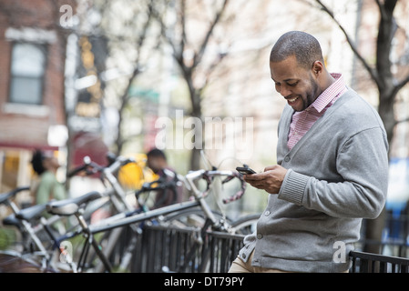 Un uomo con il suo telefono cellulare. Un gruppo di persone in background. Rack di ciclo. Foto Stock