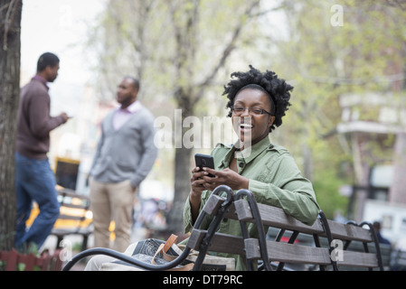 Una donna su un banco di controllo il suo telefono. Due uomini in background. Foto Stock