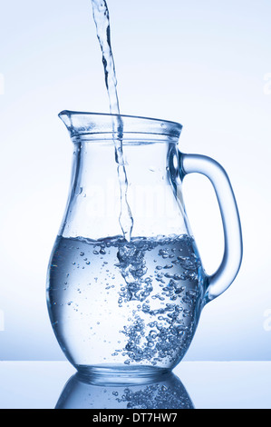 Acqua che scorre in una brocca su sfondo blu Foto Stock