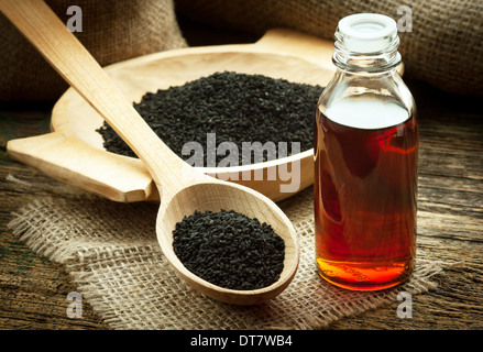 Nigella sativa (cumino nero) sul cucchiaio di legno e olio essenziale. Vero olio di nigella appare come il miele scuro Foto Stock