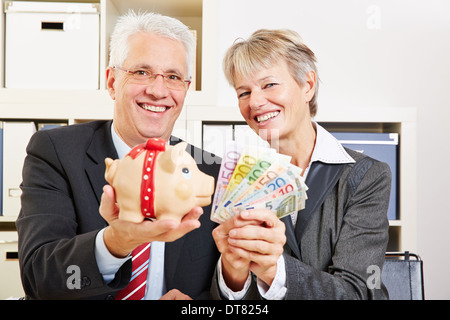 Due senior business persone azienda Euro denaro e salvadanaio in ufficio Foto Stock