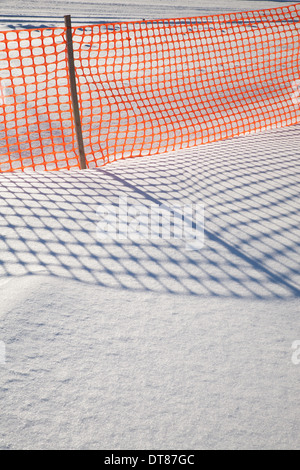 Ombre di un arancione in plastica recinzione neve fare modelli su New England neve. Foto Stock