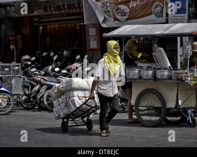 Thailandia scena di strada con un uomo che sta utilizzando un carrello a mano per offrire beni di mercato. Thailandia SUDEST ASIATICO Foto Stock