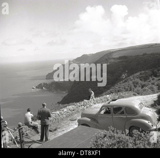 Foto storiche da anni cinquanta che mostra tre uomini adulti in cima a una scogliera che guarda sul mare e sulle colline circostanti. Foto Stock