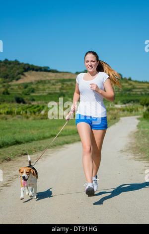 Bella ragazza adolescente jogging con il suo animale domestico (cane beagle) in natura Foto Stock