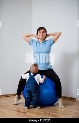 Madre esercita sul big blue montare la sfera a casa con il suo bambino Foto Stock