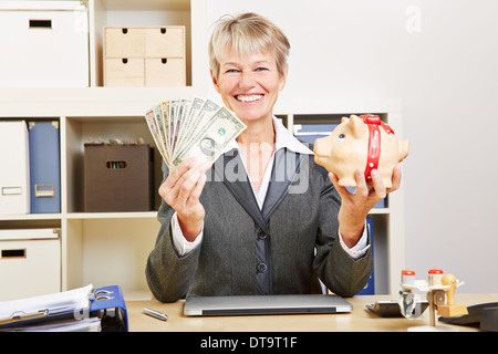 Sorridendo felice anziani business donna con le fatture del dollaro e un salvadanaio Foto Stock