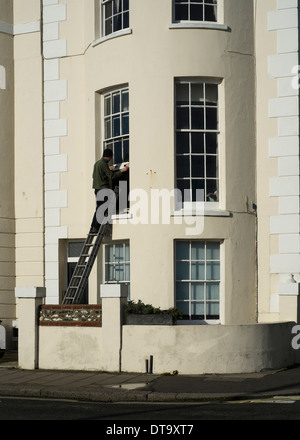 Un uomo che ripara finestre a ghigliottina su un edificio del periodo su Worthing Seafront. Foto di Julie Edwards Foto Stock