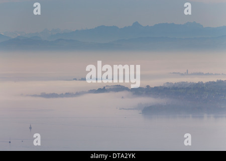 La nebbia sopra il lago di Costanza con una vista verso Dingelsdorf, Isola di Mainau, Alpi svizzere nella parte posteriore, Baden-Württemberg, Germania Foto Stock