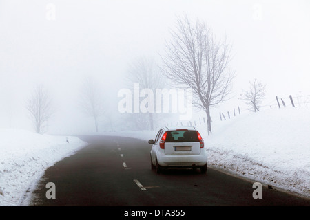 Auto sulla strada di un paese in un paesaggio ricoperto di neve, nebbia, Bergneustadt, Nord Reno-Westfalia, Germania Foto Stock