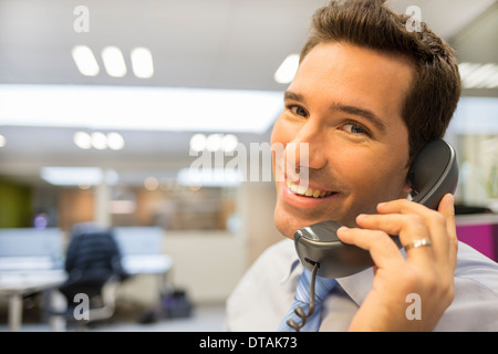 Imprenditore sorridente sul telefono in ufficio, guardando la fotocamera Foto Stock
