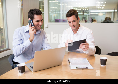 Due uomini di affari informale lavorando insieme in ufficio con computer portatili e tablet pc Foto Stock