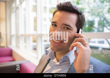 Sorridenti giovane imprenditore sul telefono in ufficio, guardando la fotocamera Foto Stock