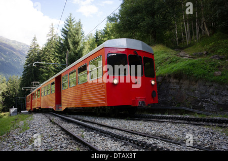 Un rosso e bianco treno del Montenvers ferrovia a cremagliera si arrampica attraverso gli alberi al di sopra di Chamonix in Francia. Foto Stock