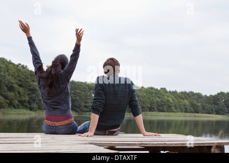 Coppia giovane seduto sul molo, vista posteriore Foto Stock