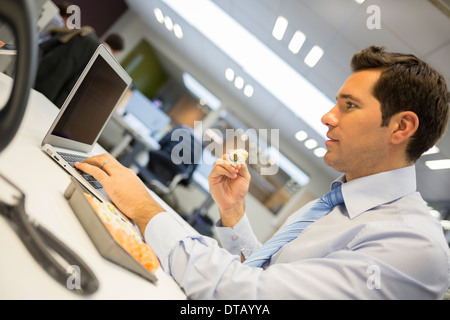 Uomo d affari con computer portatile a mangiare il sushi sulla sua scrivania Foto Stock