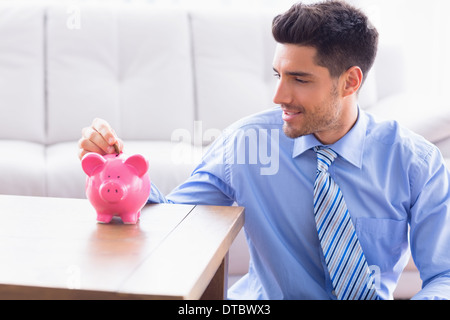 Imprenditore sorridente mettendo monete nel salvadanaio Foto Stock