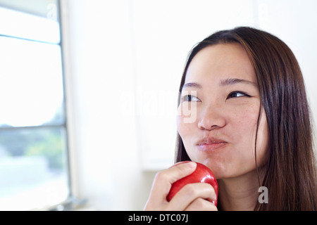 Giovane donna in cucina mangiare mela rossa Foto Stock