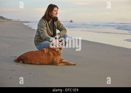 Donna matura come accarezzare il suo cane sulla spiaggia Foto Stock