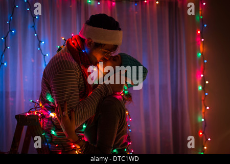 Coppia giovane kissing mentre avvolto in fairy luci di Natale Foto Stock
