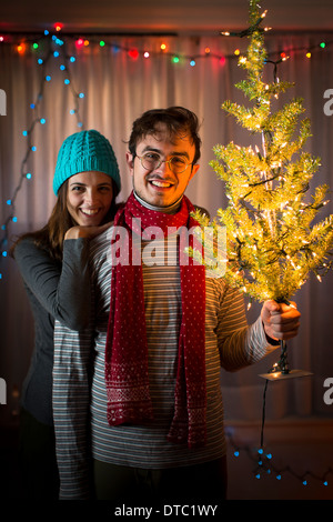 Coppia giovane azienda illuminate albero di natale Foto Stock