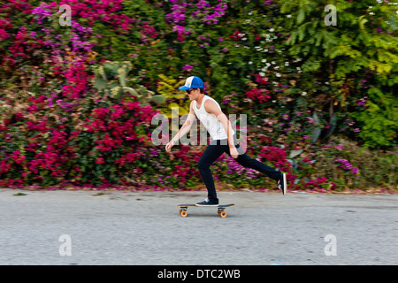 Giovane uomo lo skateboard lungo il marciapiede suburbana Foto Stock