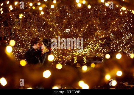 Coppia giovane kissing circondato da città delle luci di Natale Foto Stock