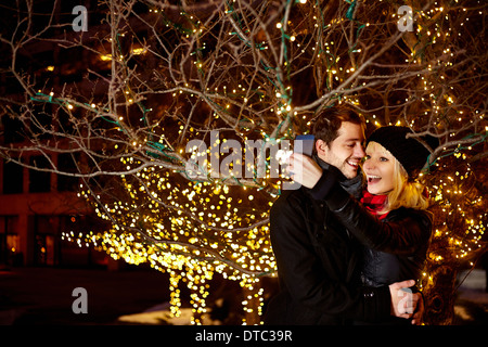 Coppia giovane tenendo autoritratto con la città delle luci di Natale Foto Stock