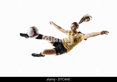 Studio shot di femmina giovane giocatore di calcio calci palla metà aria Foto Stock