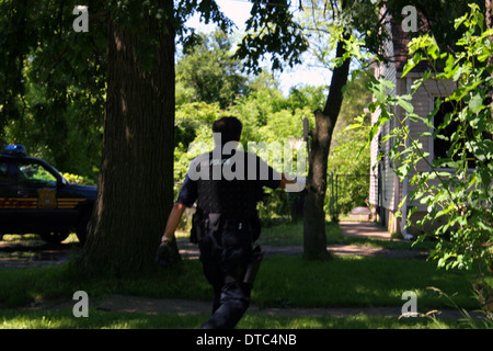 Una polizia di Detroit stupefacenti officer si muove delicatamente verso una casa con la sua pistola estratta durante un raid. Foto Stock