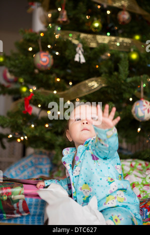 Baby girl raggiungendo fino, l'albero di natale in background Foto Stock