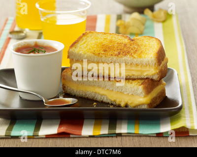 Formaggio alla griglia in sandwich con una tazza di zuppa di pomodoro e un bicchiere di succo di arancia in background. Foto Stock