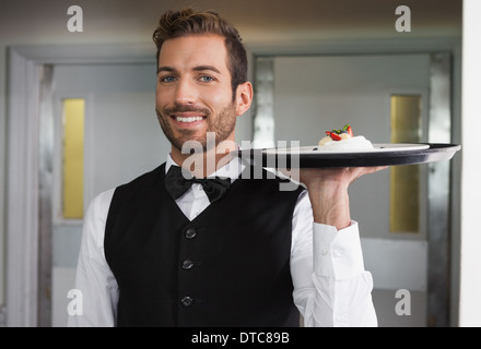 Sorridente cameriere tenendo il vassoio con la piastra di dessert Foto Stock