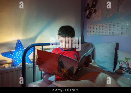 Ragazzo giovane,la lettura di una storia prima di addormentarsi nel suo letto Foto Stock