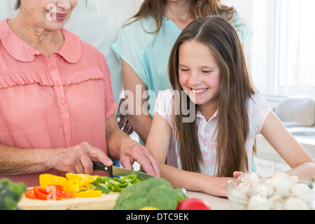 Ragazza guardando la nonna tagliare le verdure Foto Stock