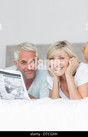 Sorridente Coppia matura leggendo il giornale in bed Foto Stock