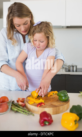 La madre ad assistere la ragazza di trinciatura di capsicum Foto Stock