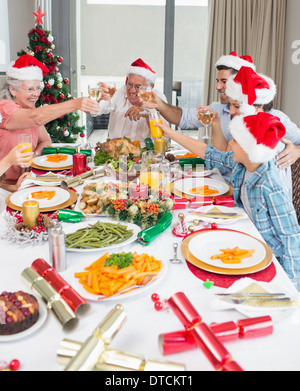 La famiglia in cappelli di Babbo Natale tostatura di bicchieri di vino al tavolo da pranzo Foto Stock