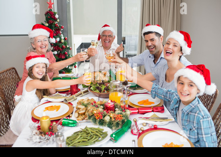 La famiglia in cappelli di Babbo Natale tostatura di bicchieri di vino al tavolo da pranzo Foto Stock