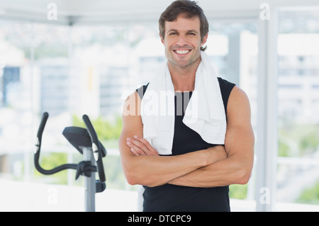 Uomo sorridente in piedi con le braccia incrociate a lezione di spinning in palestra luminosa Foto Stock