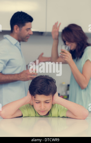 Triste giovane ragazzo che copre le orecchie mentre i genitori quarreling Foto Stock