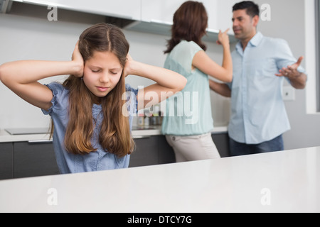 Ragazza triste che copre le orecchie mentre i genitori quarreling in cucina Foto Stock