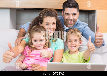 La famiglia felice seduto sul divano utilizzando laptop dando pollice in alto Foto Stock