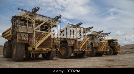 Hitatchi massiccia e Komatsu Mining haul camion parcheggiato fino in una linea in un cielo aperto e di rame miniera d'oro. Foto Stock