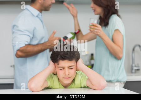 Triste giovane ragazzo che copre le orecchie mentre i genitori quarreling Foto Stock