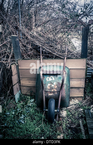 Carriola in metallo arrugginita appoggiata contro il cumulo di composto all'assegnazione inverno Foto Stock