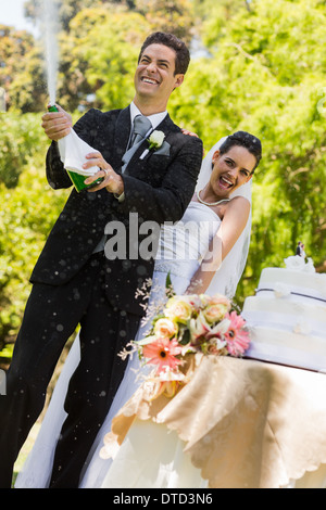 Sposa giovane con lo sposo di aprire la bottiglia di champagne al park Foto Stock