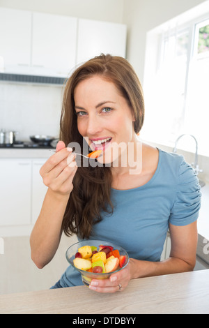 Sorridente giovane donna di mangiare insalata di frutta in cucina Foto Stock