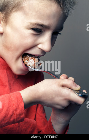 Ragazzo (6-7) mangiare il cioccolato con il cucchiaio. Foto Stock