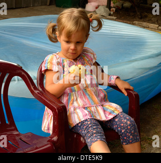 Due-anno-vecchia ragazza una mela nella sedia da giardino Foto Stock